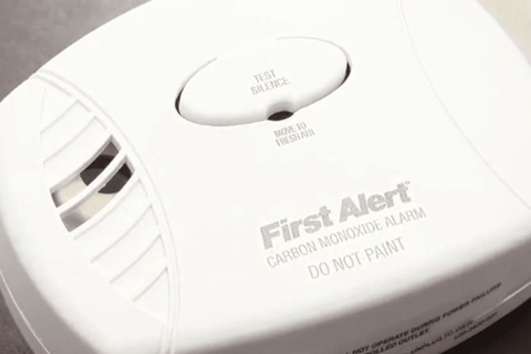 Close-up of a First Alert carbon monoxide alarm with "TEST/SILENCE" button and warning text "DO NOT PAINT" visible on the device.