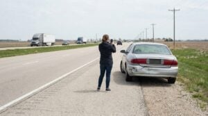 person photographing damaged sedan pulled over on highway shoulder after collision